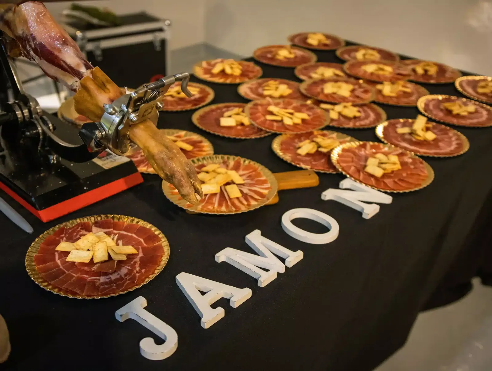Mesa con platos de jamón cortado a cuchillo y regañás en una celebración en LA NAVE 77